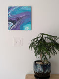 abstract liquid acrylic paint on 12x12" canvas, blues, greens and purples mix and flow in endless movement, can display in various directions, pictured pn wall over table
