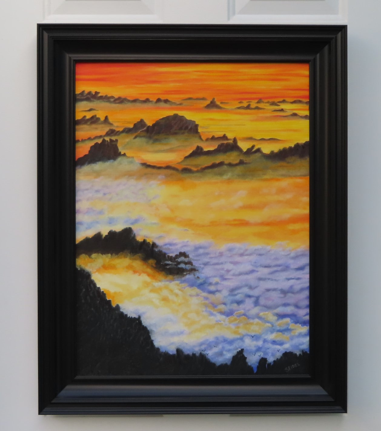 18" wide x 24"tall original oil painting of brilliant sunset sky with mountains rising out of layers of clouds, framed in modern black frame