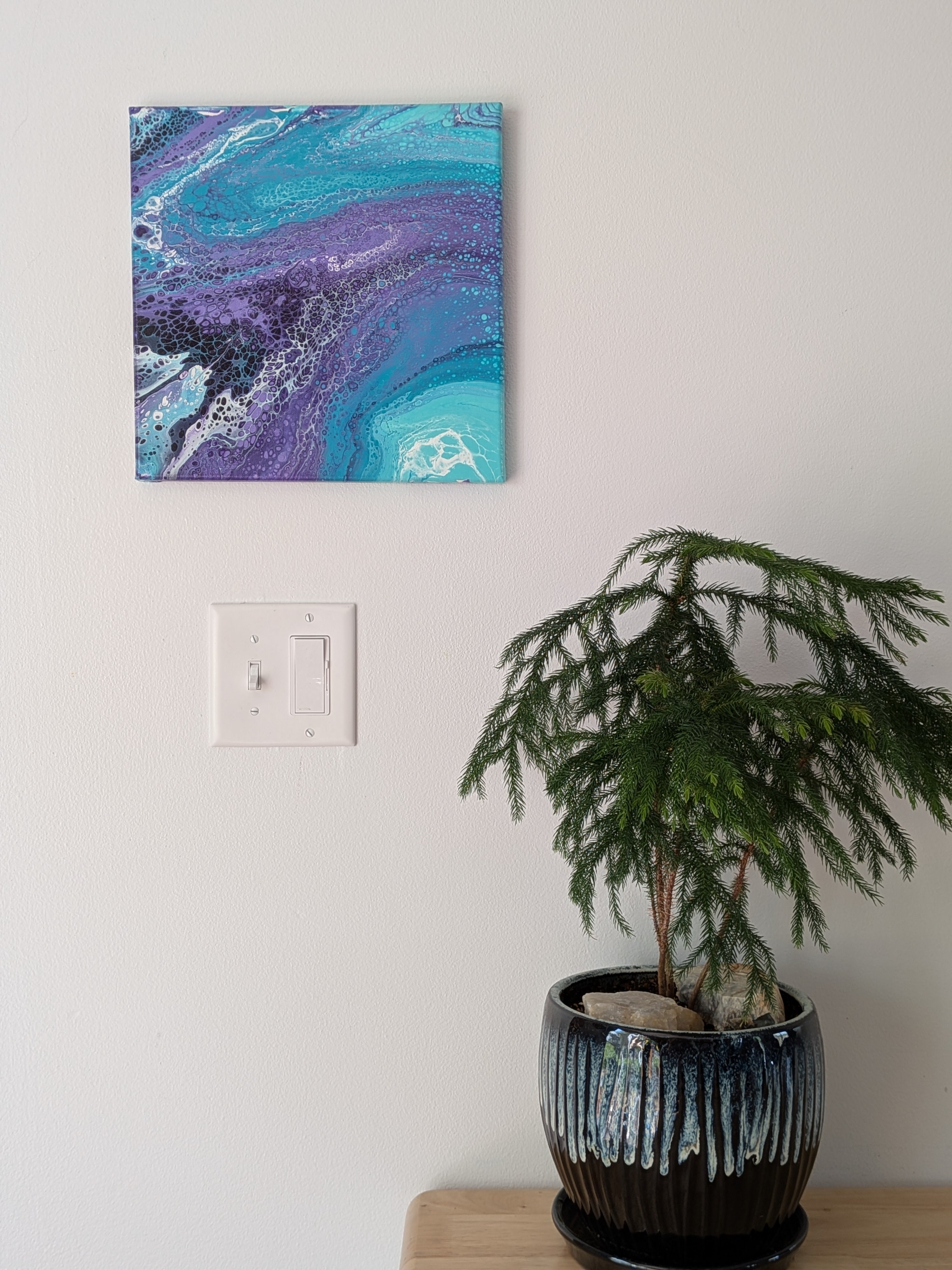 abstract liquid acrylic paint on 12x12" canvas, blues, greens and purples mix and flow in endless movement, can display in various directions, pictured pn wall over table