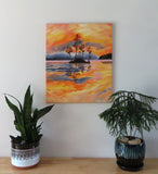 Original oil painting of a colorful pastel sky, the oranges, yellows and pinks contrast with the distant hills rising out of the mist and the dark silhouetted island and trees reflected in calm waters 24" tall by 20" wide unframed; shown over aa table with plants