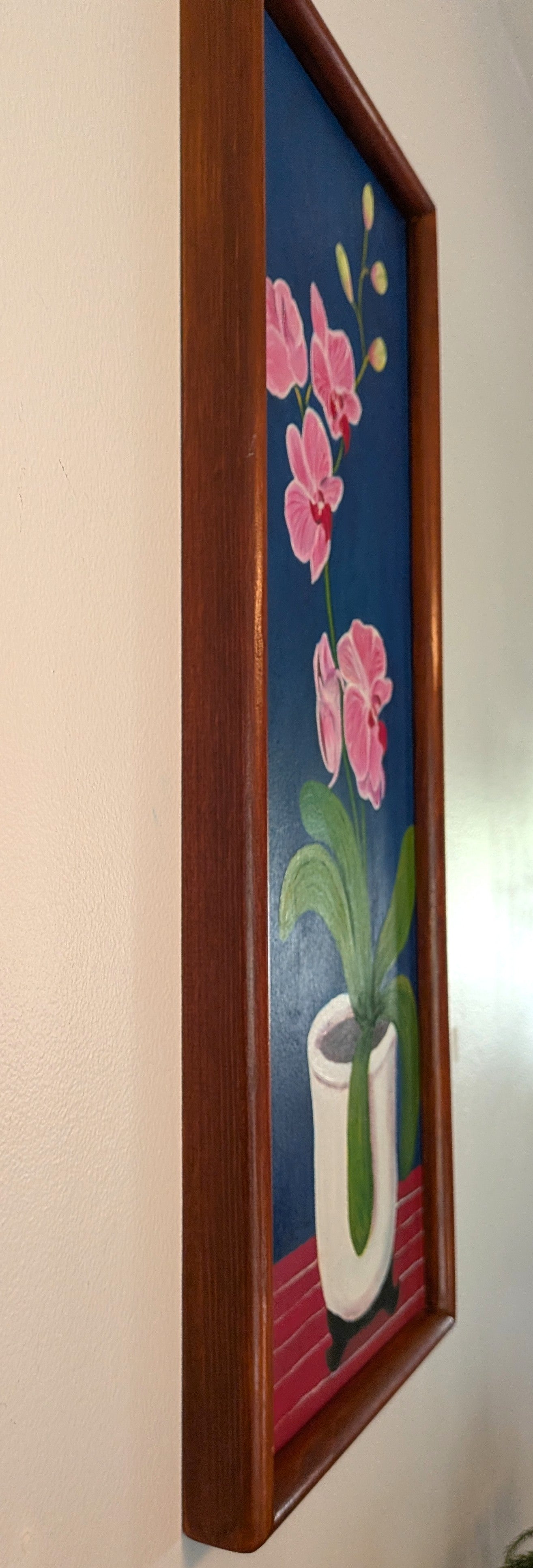 original oil painting on board of pink orchids against a royal blue background, in a white pot, framed in a handmade red chestnut colored frame, a left side view to show the depth of the frame