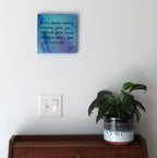 8x8" abstract painting on canvas with liquid acrylics, blues and purples with gold accent and inspirational quote, shown over secretary-desk