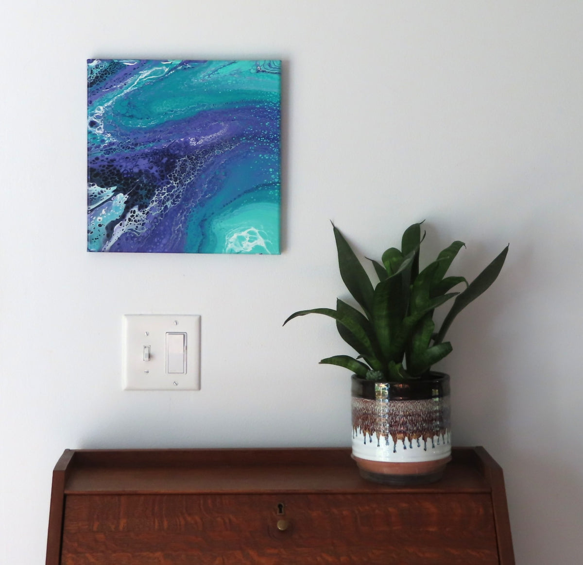 abstract liquid acrylic paint on 12x12" canvas, blues, greens and purples mix and flow in endless movement, can display in various directions, shown here over a secretary-desk.