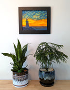 original oil painting of Erie Pierhead light house silhouetted by beautiful sunset and clouds, painted on 11 x 14 canvas panel, framed in modern black frame, displayed on wall over table