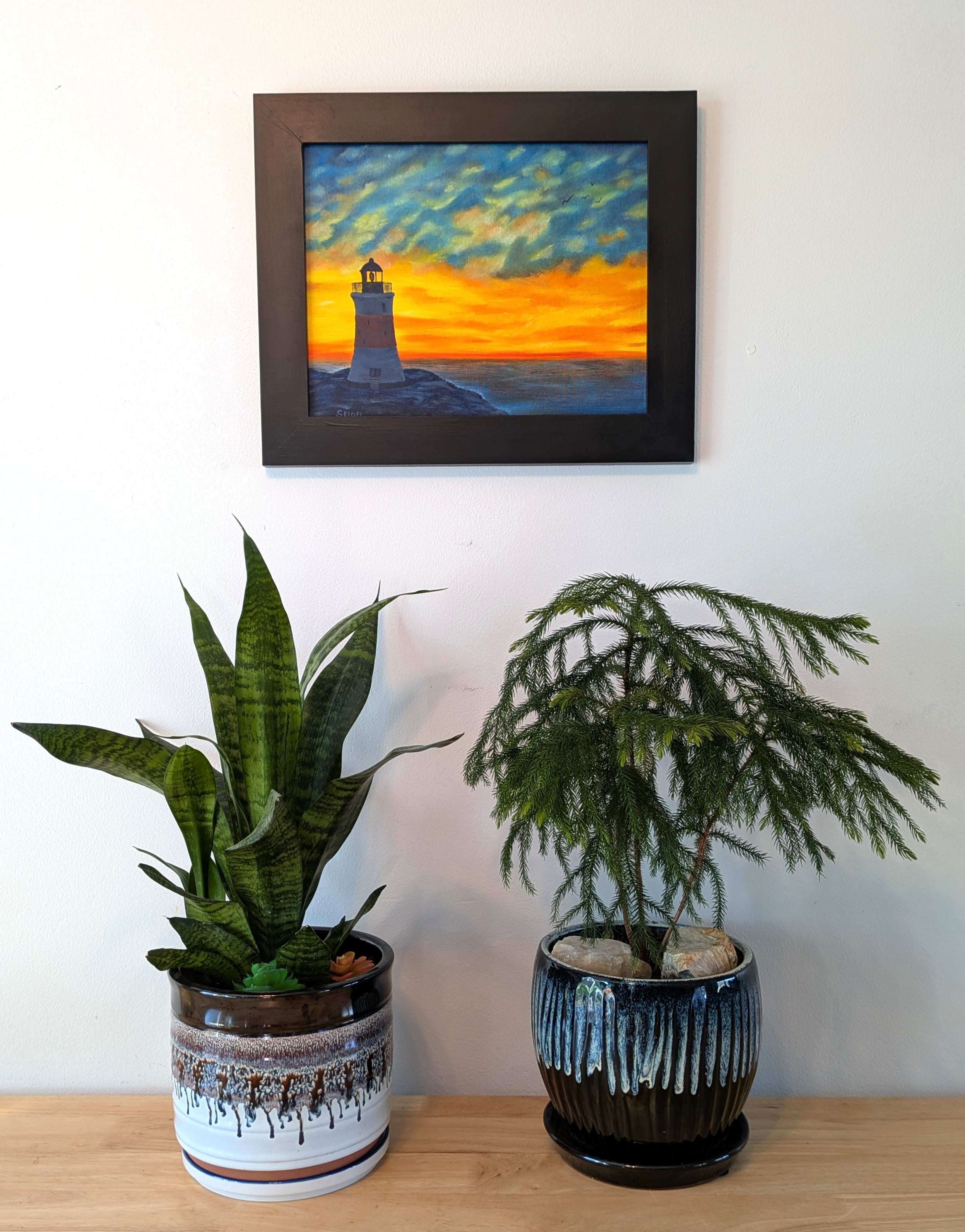 original oil painting of Erie Pierhead light house silhouetted by beautiful sunset and clouds, painted on 11 x 14 canvas panel, framed in modern black frame, displayed on wall over table