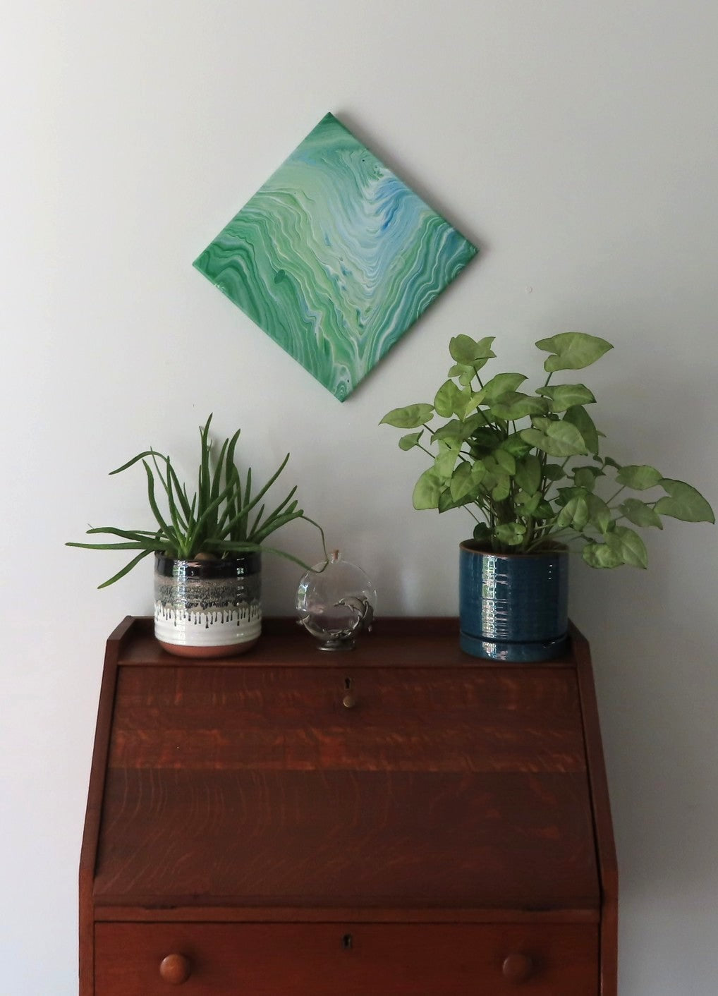 This original liquid art painting is a 12 x 12" abstract on canvas. It can be displayed in any direction. The green with white and blue accents are mesmerizing and calming. It is shown here in a diamond display.