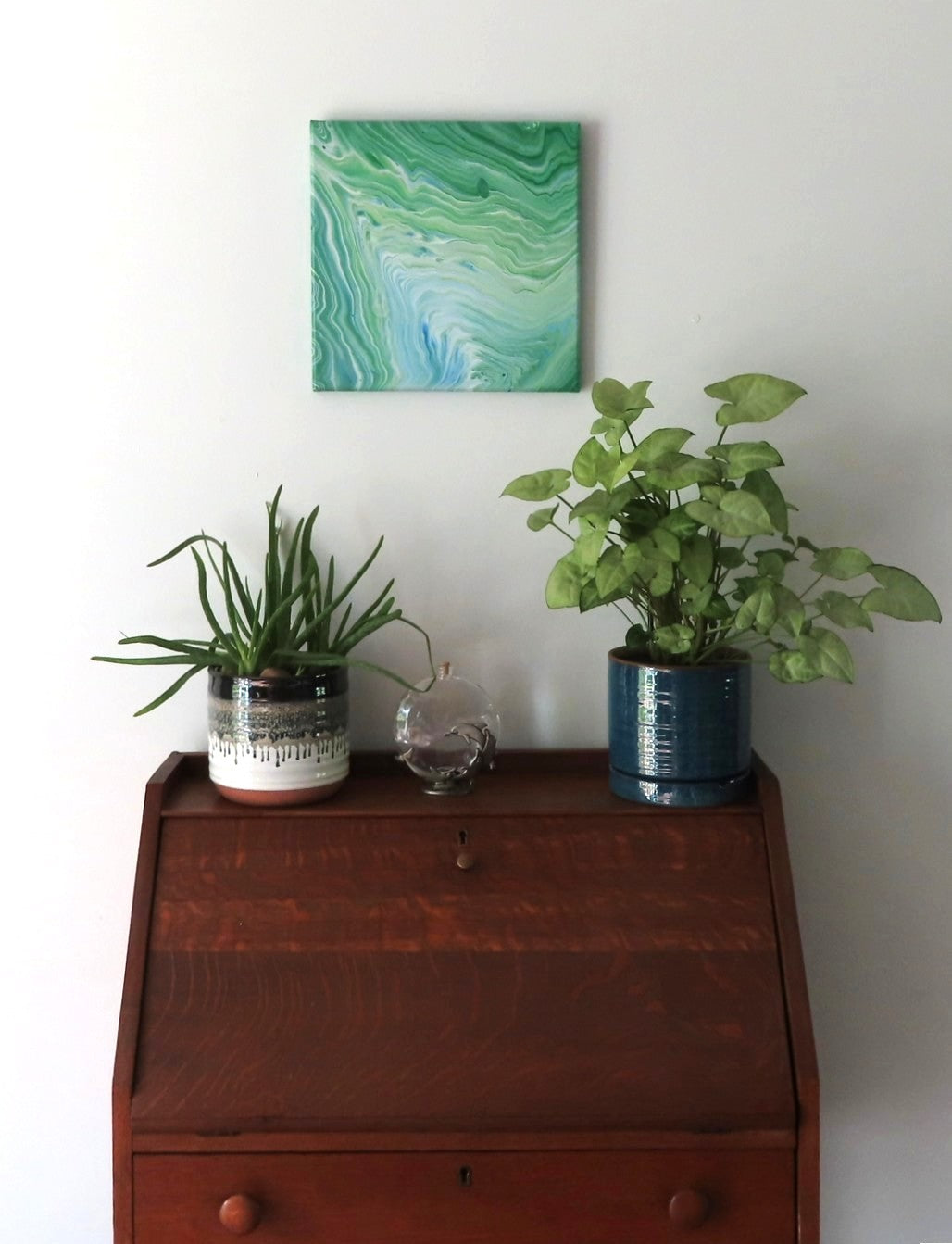 This original liquid art painting is a 12 x 12" abstract on canvas. It can be displayed in any direction. The green with white and blue accents are mesmerizing and calming. It is shown here over a secretary desk in an alternate display.