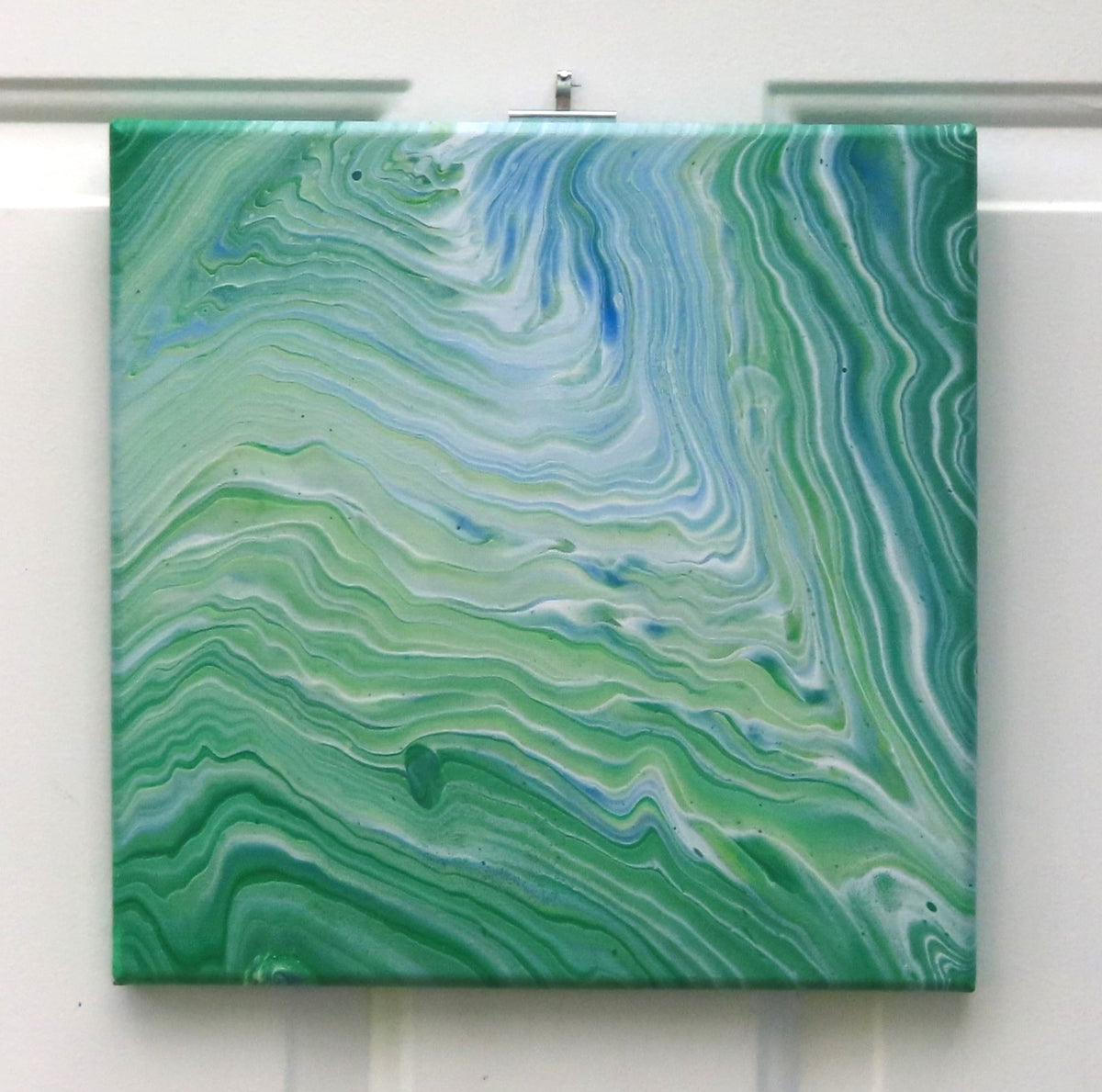 This original liquid art painting is a 12 x 12" abstract on canvas. It can be displayed in any direction. The green with white and blue accents are mesmerizing and calming.