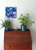 original abstract poured acrylic painting on 12x12" canvas, bright swirling purples, white and rich blues seem energetic, shown here in an alternate direction over a secretary desk