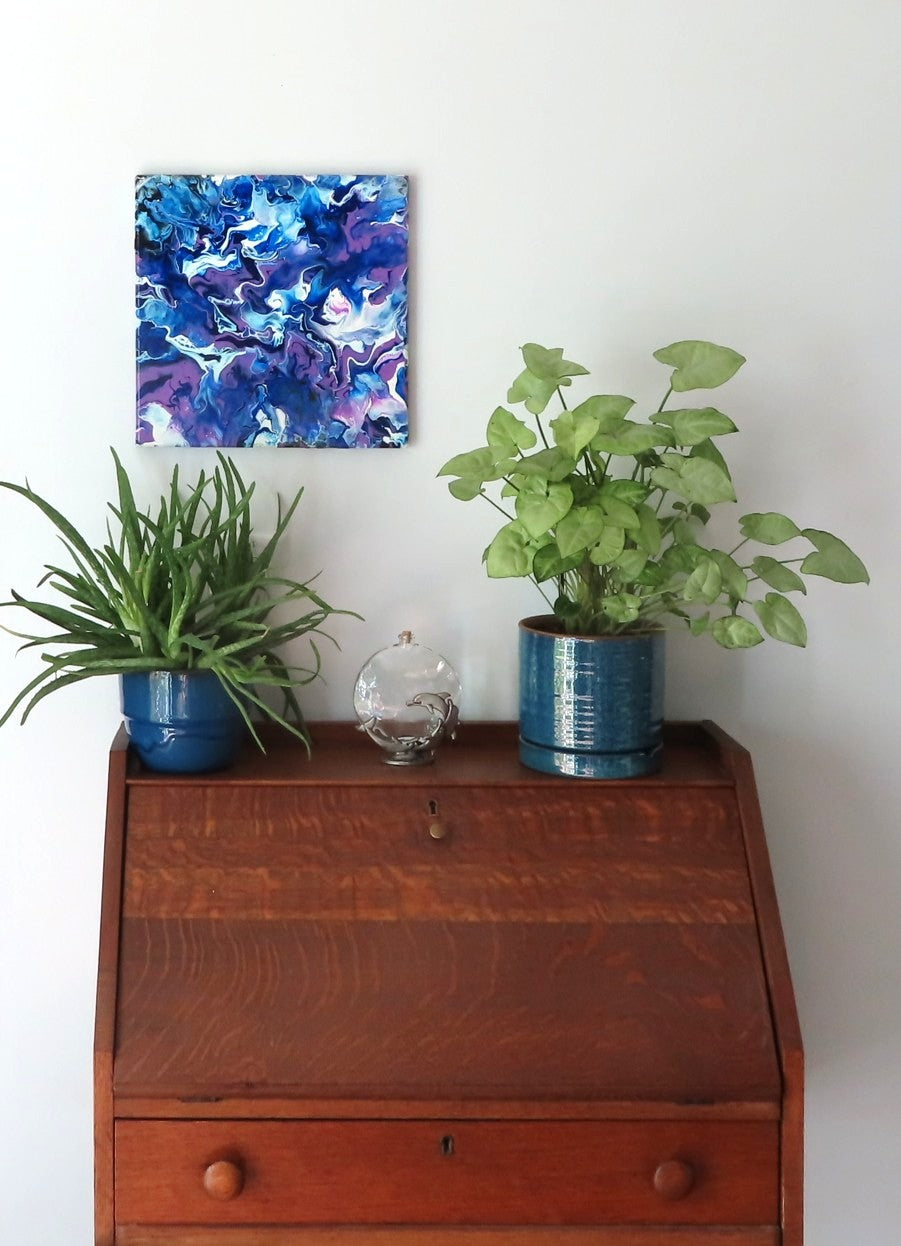 original abstract poured acrylic painting on 12x12" canvas, bright swirling purples, white and rich blues seem energetic, shown here in an alternate direction over a secretary desk