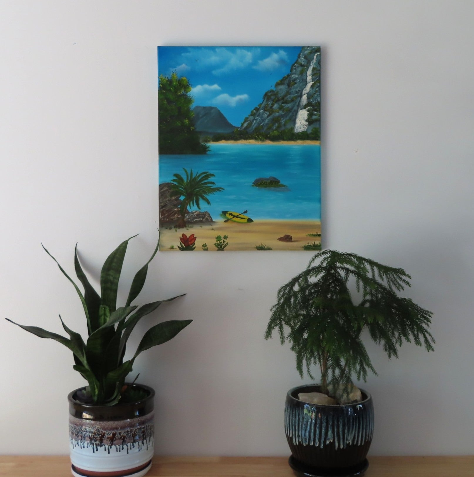 original oil painting of lovely blue water, beach and waterfall surrounding a cove with kayak, unframed, displayed over table