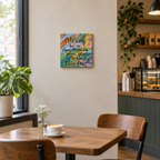 An 8x8" original abstract acrylic painting with multicolored swirls and a textual inspirational quote that reads 'NEVER BE SO OPEN-MINDED THAT YOUR BRAIN FALLS OUT'. Shown in a cafe.