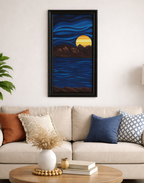 original oil painting, 12 x 24 in an abstracted style, of a bright colored planet rising over the horizon in another world cool blue sky and water framed in black shown over sofa
