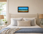 12x24 original oil painting of ocean, waves, sailboats, paragliders, and sandy beach, framed in black, displayed over bed