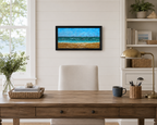 12x24 original oil painting of ocean, waves, sailboats, paragliders, and sandy beach, framed in black, displayed behind desk