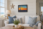 11x14" colorful sunset over ocean, rocky coast, lighthouse, shown over a sofa in seaside cottage