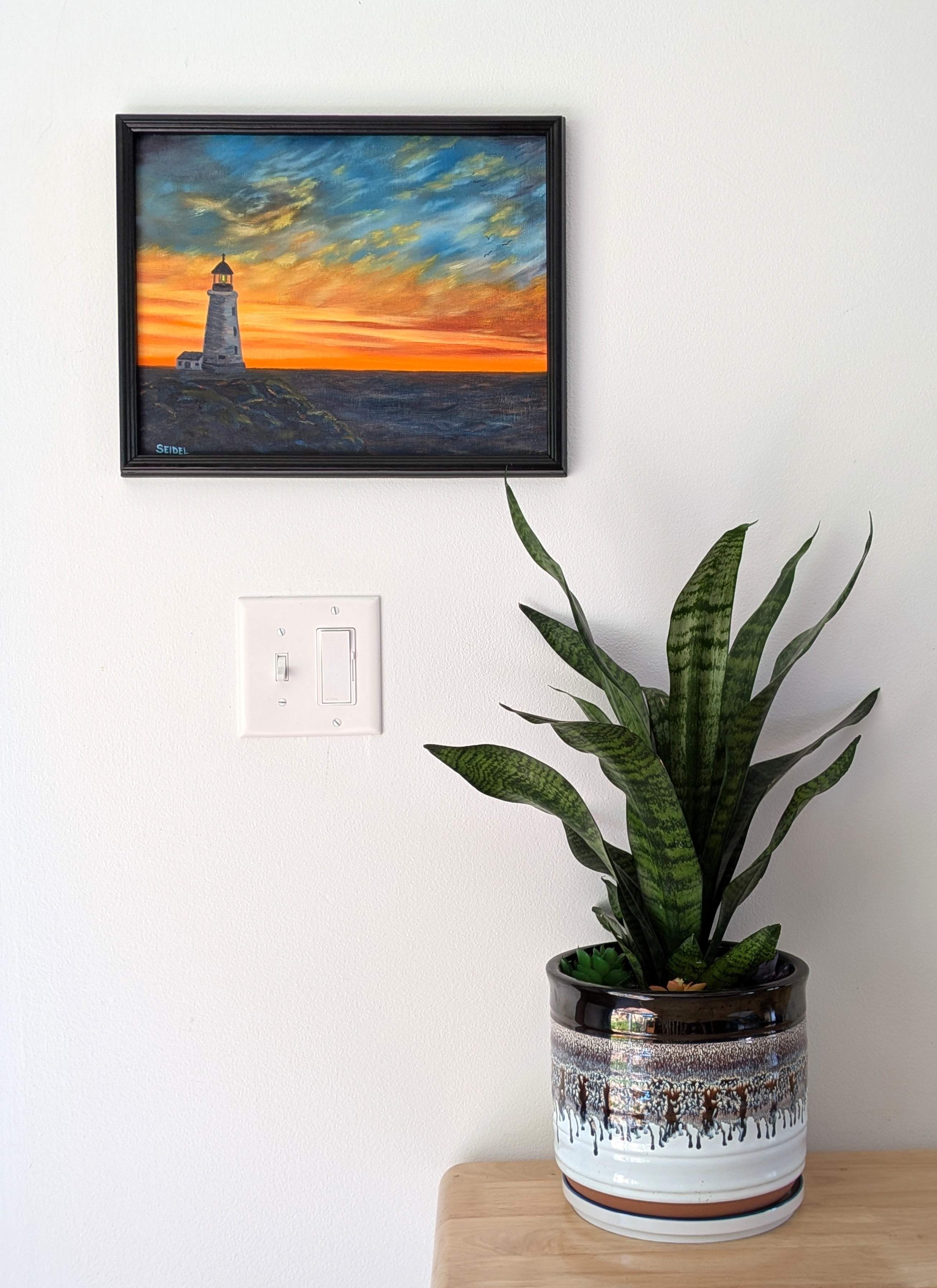 11x14" original oil painting, lighthouse, rocky shore, colorful sunset, framed pictured over table