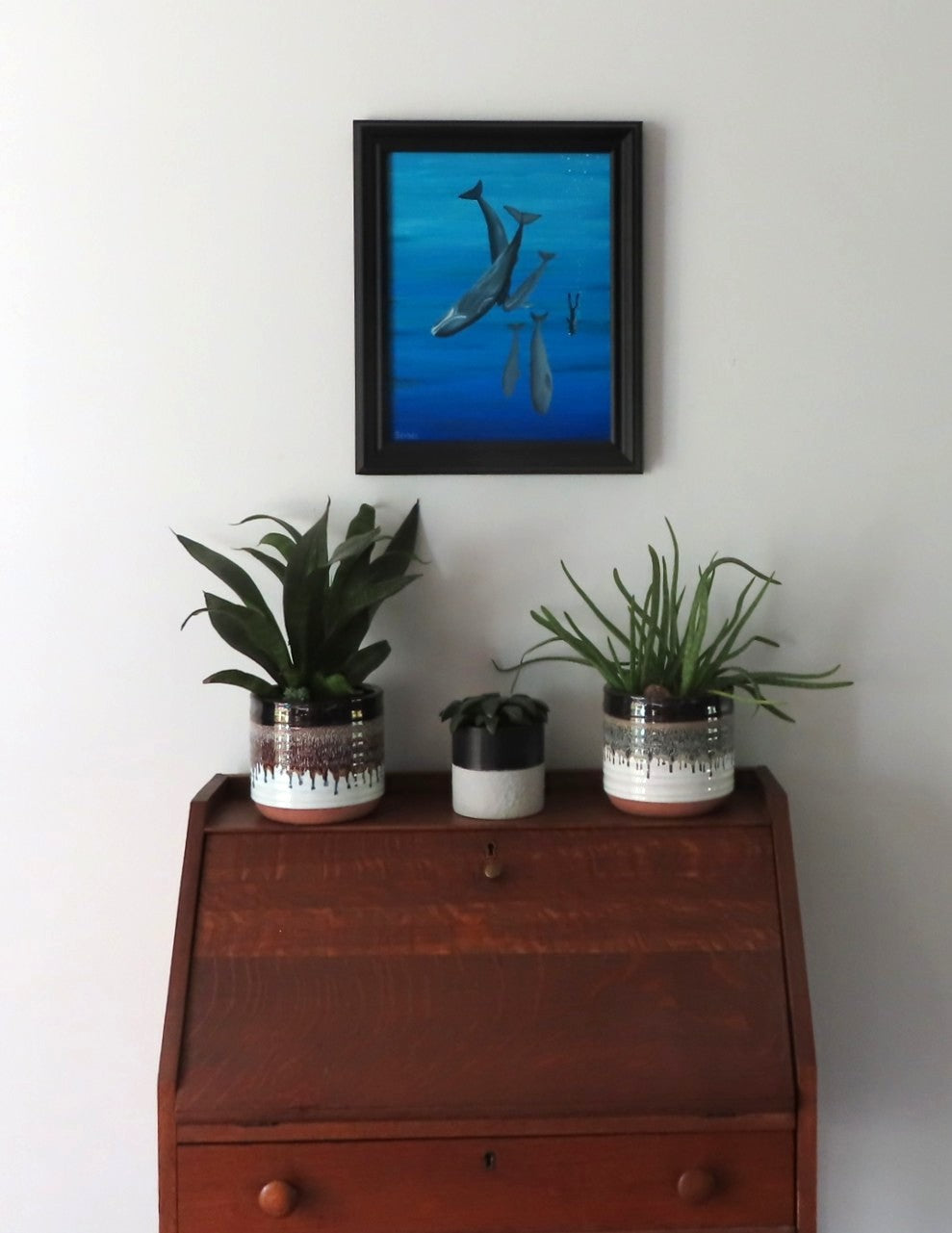 11x14 original oil painting of a scuba diver swimming with whales, framed in black, shown over a secretary desk