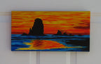 7x14" original acrylic painting of a brilliant sunset on ocean with large silhoutted sea stacks, shown on white wall
