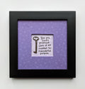 An 8x8" original framed artwork with a purple background and a black frame, featuring a textual message 'You are a work of art' alongside a key.