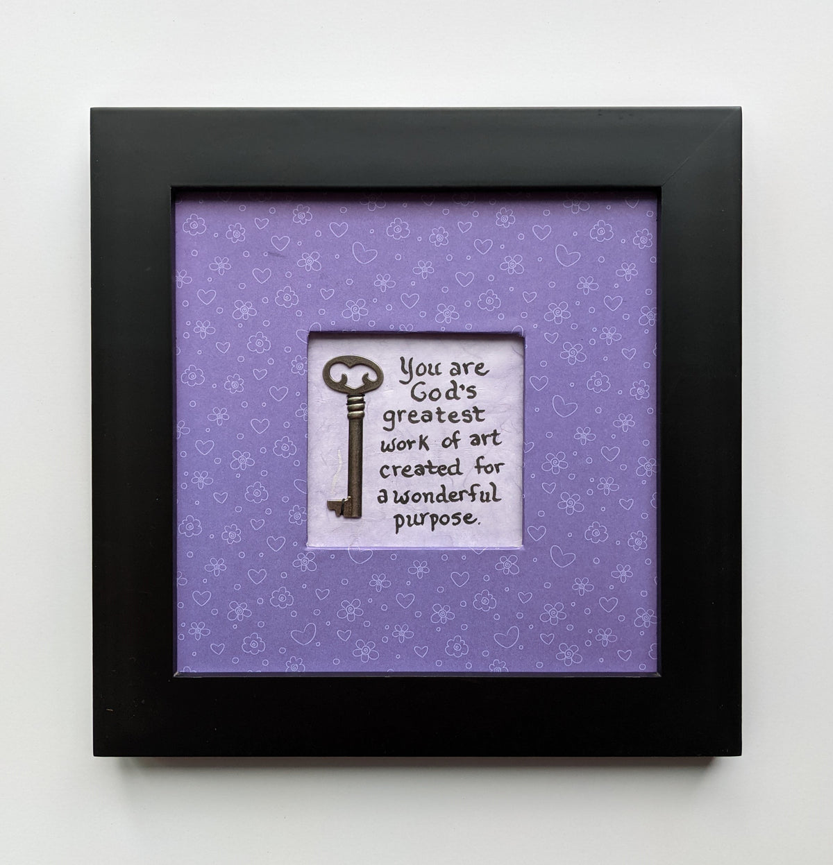 An 8x8" original framed artwork with a purple background and a black frame, featuring a textual message 'You are a work of art' alongside a key.