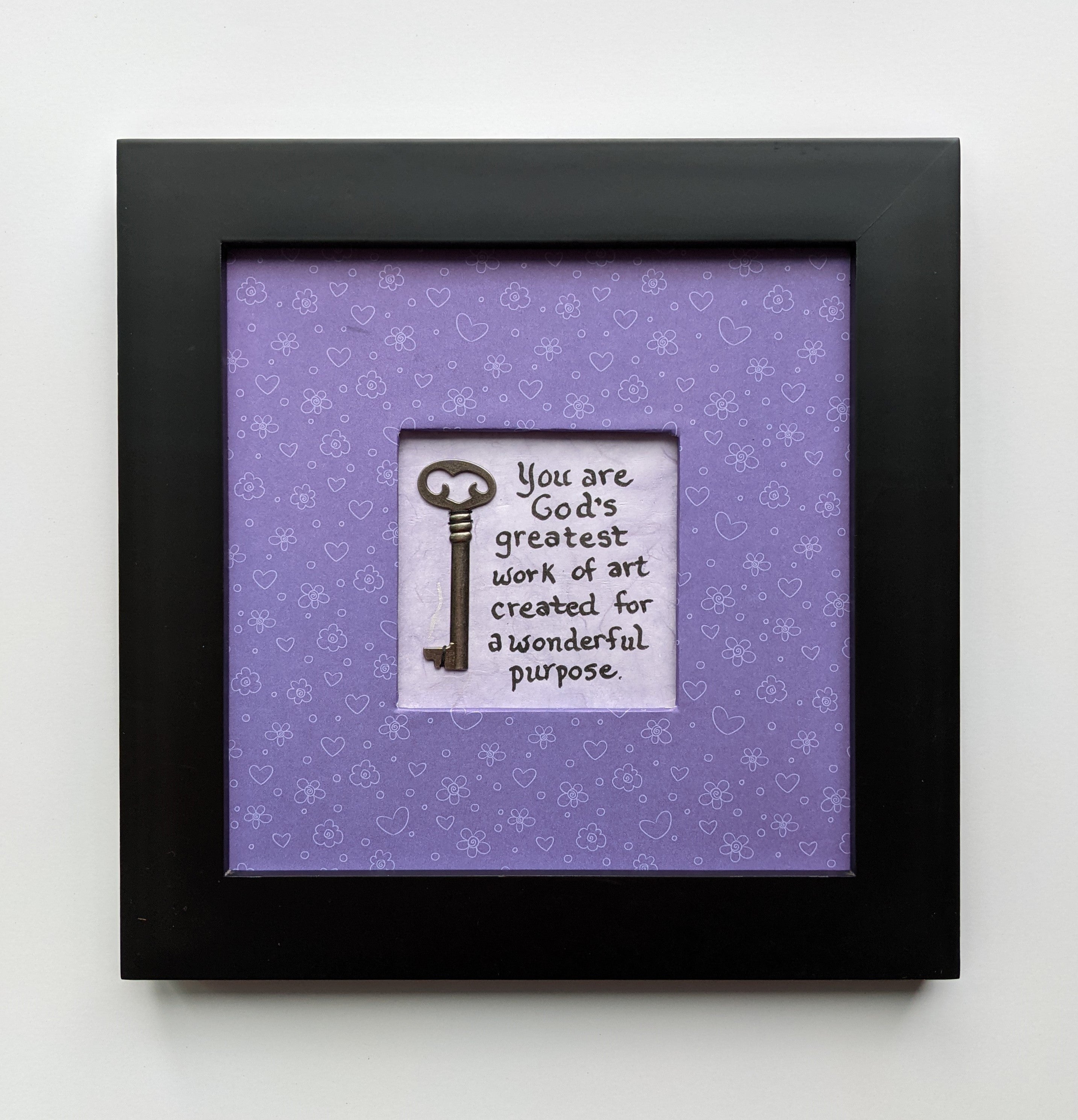 An 8x8" original framed artwork with a purple background and a black frame, featuring a textual message 'You are a work of art' alongside a key.